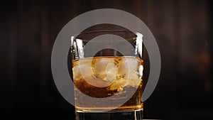 Close-up of a glass of whiskey with ice spinning around on a wooden background.