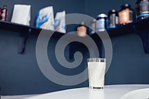 Close up of glass with white cocktail and straw. Protein shake on the counter in sports bar. Banks with sports nutrition on