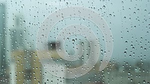 Close up of a glass window on a rainy day with big drops on blurred city and grey heavy sky background. Stock footage