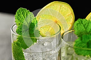Close-up glasses of mojito cocktail with mint and lime and ice on a dark background. Side view