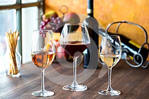 Glasses of rose, red and white wine on a wooden table.