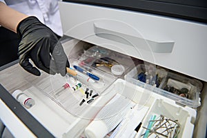 Close-up gloved hand of dentist taking out dental tool form the drawer with dental instruments, consumables and supplies