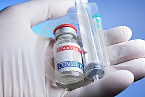 close up of gloved hand holding coronavirus vaccine vial, syringe and needle