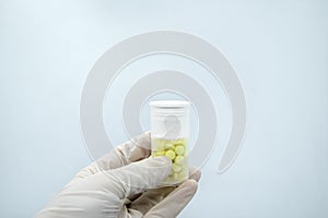 Close-up of gloved hand holding transparent pill bottle on white background
