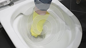 Close-up of a gloved hand using a washcloth while cleaning the toilet bowl in the bathroom