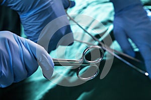 Close-up of gloved hands holding the surgical scissors and working, operating room, hospital photo