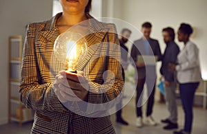 Close up of glowing Edison light bulb in hands of woman who holds it in business office.