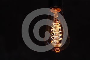 Close up glowing light bulb. Vintage lightbulb on dark background with bright yellow shining wire
