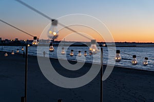 Close up of the glowing light bulbs at the beach cafe terrace. Sun is setting in the blurry abstract background.