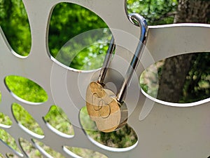 Close-up. Gold-colored lock with hearts hangs on an iron fence on a summer day. The concept of family, love and fidelity