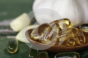 Close up of gold garlic extract capsules oil in wooden spoon