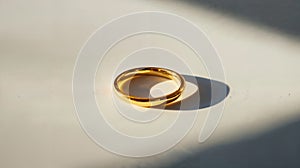 Close-up of a gold wedding ring casting a shadow on a white surface.