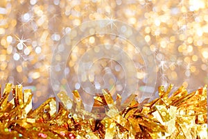 Close-up golden shiny tinsel down in foreground on background of golden bokeh with asterisks and copy space.