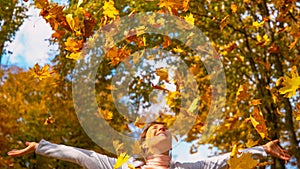 CLOSE UP: Golden tree leaves fall onto playful woman after throwing them in air