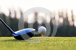 Close up golf ball and driver, player doing golf swing tee off on the green sunset evening time,