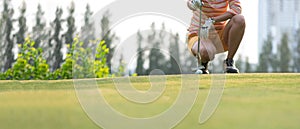 Close up golf ball woman putting golf ball in hole tee with club in golf course on evening on time for healthy sport.