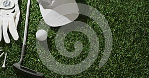 Close up of golf club, ball, glove and peaked cap on grass, copy space, slow motion