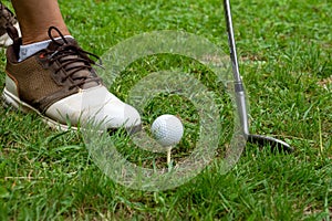 Close-up of golf club and cue ball on tee, and man`s foot with golf shoe, horizontally