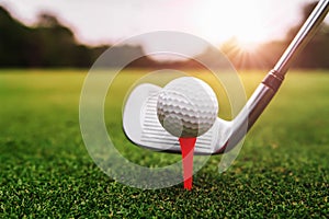 close up golf club and golf ball on green grass with sunrise background