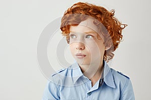 Close up of good-looking little boy with red curly hair and freckles looking aside with interested and relaxed