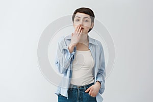 Close up of good-looking young student girl closing mouth with hand, being surprised with news her friends broke up last