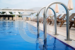 Close up of grab bars outdoor swimming pool entrance with sunlounger chairs terrace in the background