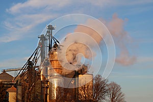 Close-up of grain dryer with bins blowing out steam at sunset