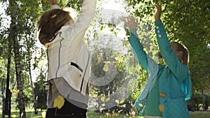 Close-up of grandmother and granddaughter tossing leaves, jumping and spinning around. Two happy caucasian women having