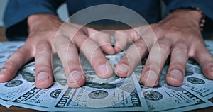 Close-up of greedy man's hands grabbing a bunch of dollars lying on the table. The man takes his money, American