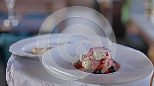 Close-up Greek salad on white plate on tray in hand of unrecognizable waiter walking in slow motion. Tasty healthful