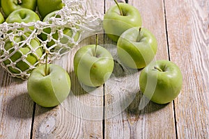 Close-up green apples and cotton string mesh bag on a wooden table. Copy space