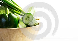 Close-up of green bell pepper, celery and cucumbers in wooden bowl over white background