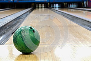 Close-up of green bowling ball against background of empty lanes in bowling alley