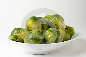 Close-up of green Brussels sprouts on a white plate, white background, horizontal
