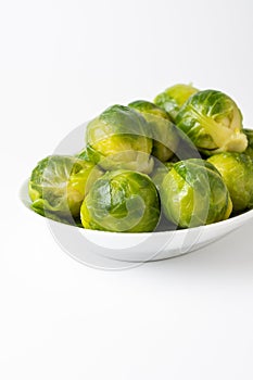 Close-up of green Brussels sprouts on white plate, white background, vertical,