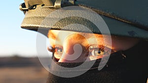 Close up green eyes of female ukrainian army soldier looking at sunset. Sight of young military woman in helmet and