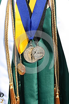 Close up of green high school graduation gown with honors medallions, tassles and sash.
