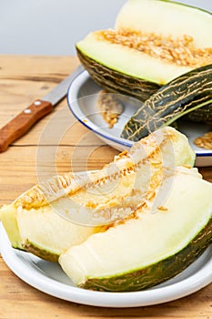 Close-up of green melon slices in white plate on wooden table, with half a melon, selective focus,