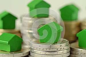 Close-up of green miniature houses on coin stacks - Concept of real estate investment, mortgage, home insurance and loan, eco-