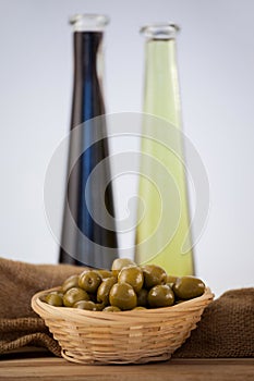 Close up of green olives in wicker basket by oil bottles