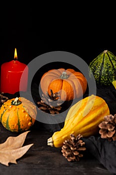 Close-up of green and orange pumpkins, with autumn leaves, pine cones and burning orange candle, selective focus, on dark wooden t