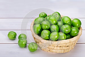 Close Up Of Green Plums Or Greengage In A Basket Isolated On White Wooden Background, Popular Spring Fruits With A Very Sharp Sou