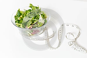 Close up green vegetables salad in glass bowl, tailor measuring tape isolated on white background. Proper nutrition