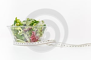 Close up green vegetables salad in glass bowl, tailor measuring tape isolated on white background. Proper nutrition