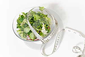 Close up green vegetables salad in glass bowl, tailor measuring tape isolated on white background. Proper nutrition