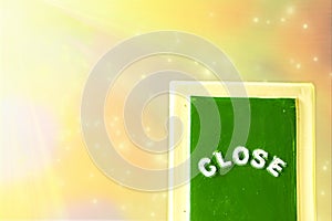 Close up of a green with yellow `CLOSE` chalkboard sign leaning against  bright, colorful with sparkly background.