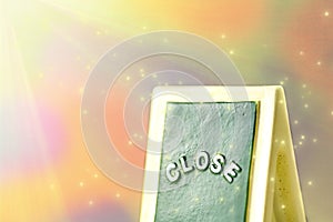 Close up of a green with yellow `CLOSE` chalkboard sign leaning against  bright, colorful with sparkly background.