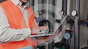 Close up of grey bearded man standing with laptop at technical plant room