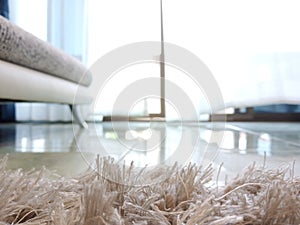 Close up grey fur carpet with blurred upholster seat and natural light from window background.