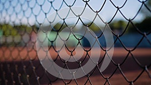 Close-up of the grid enclosing the tennis court. Silhouettes of people playing tennis are visible